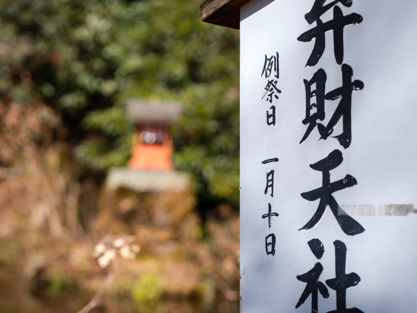 Panneau blanc calligraphié d'un petit sanctuaire japonais : 弁財天社 et, sur le côté, 例祭日 一月十日, la date de la fête annuelle écrite en chiffres kanji