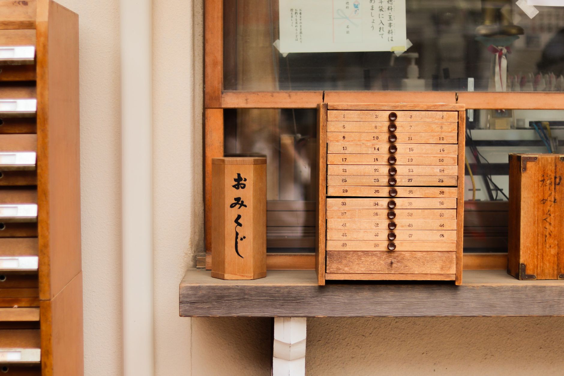 Boîte à omikuji en bois marquée おみくじ et petit meuble à tiroirs numérotés posés sur une étagère
